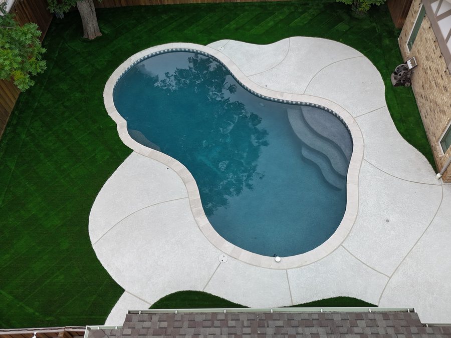 Drone view of a freeform pool with a tanning ledge and curved deck set in a lawn