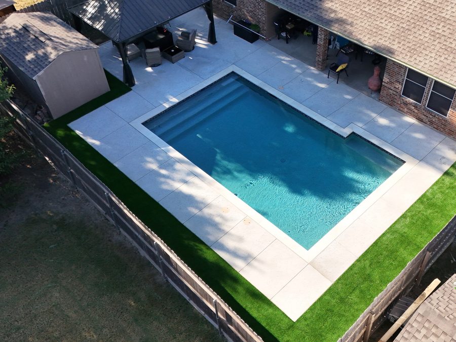 Aerial view of a rectangular pool with a wide concrete deck and covered patio
