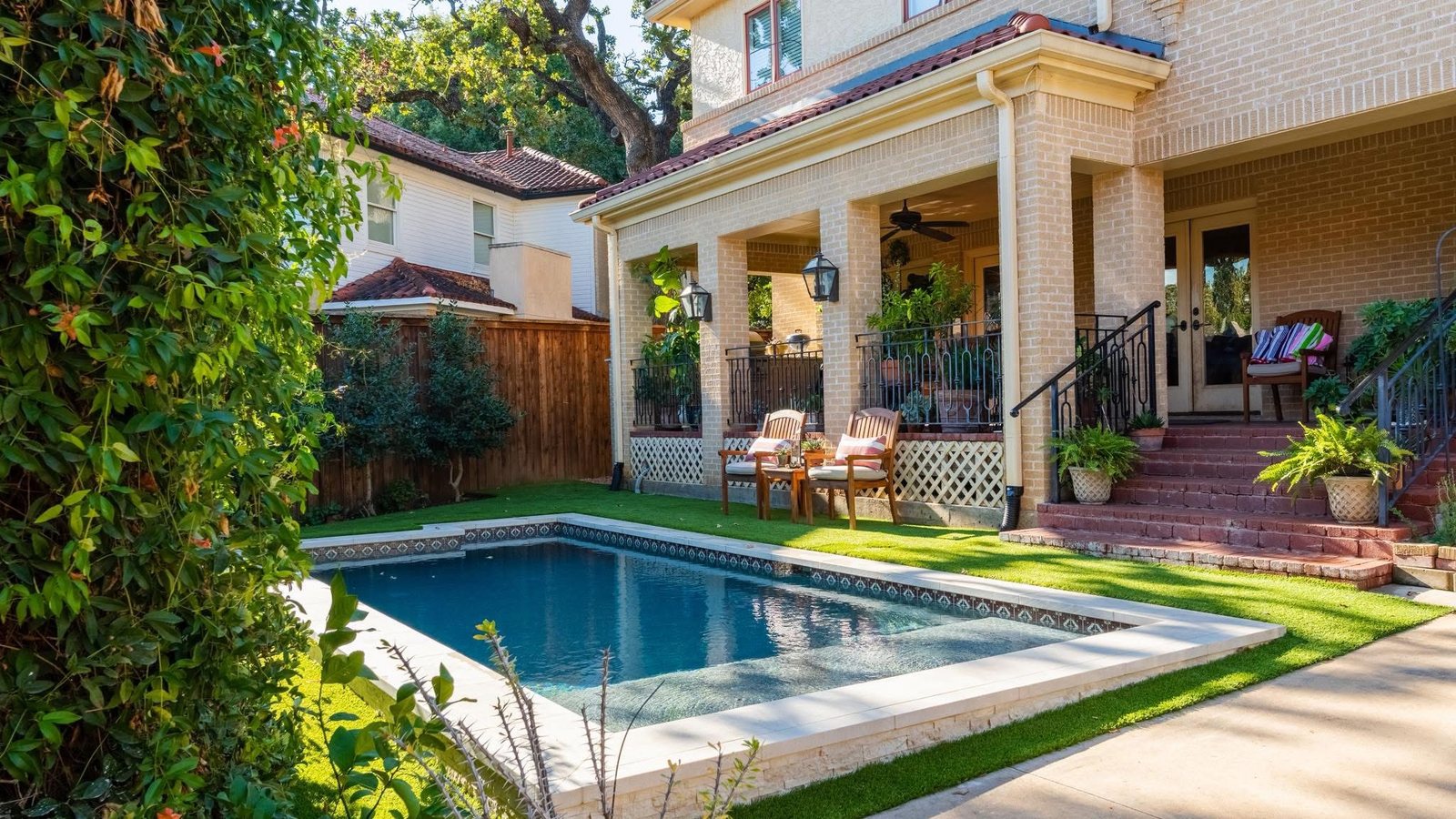 A rectangular backyard pool with a tiled edge and green lawn beside a brick home with a covered patio in Fort Worth